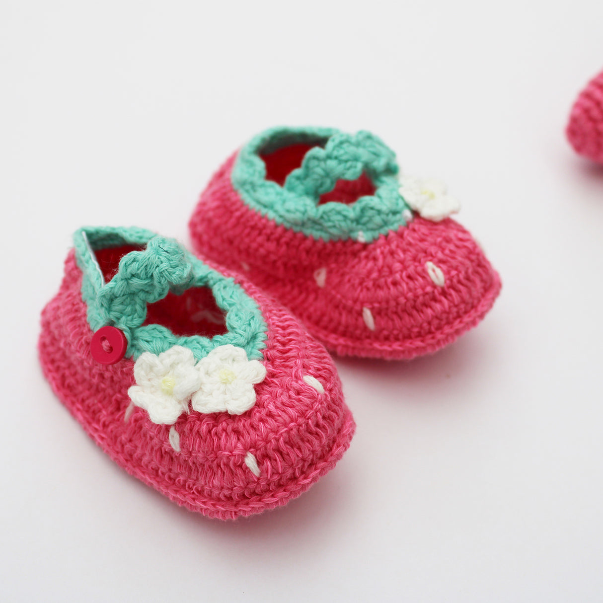 Pair of pink crochet Strawberry baby booties with green tops and white flowers on a white background