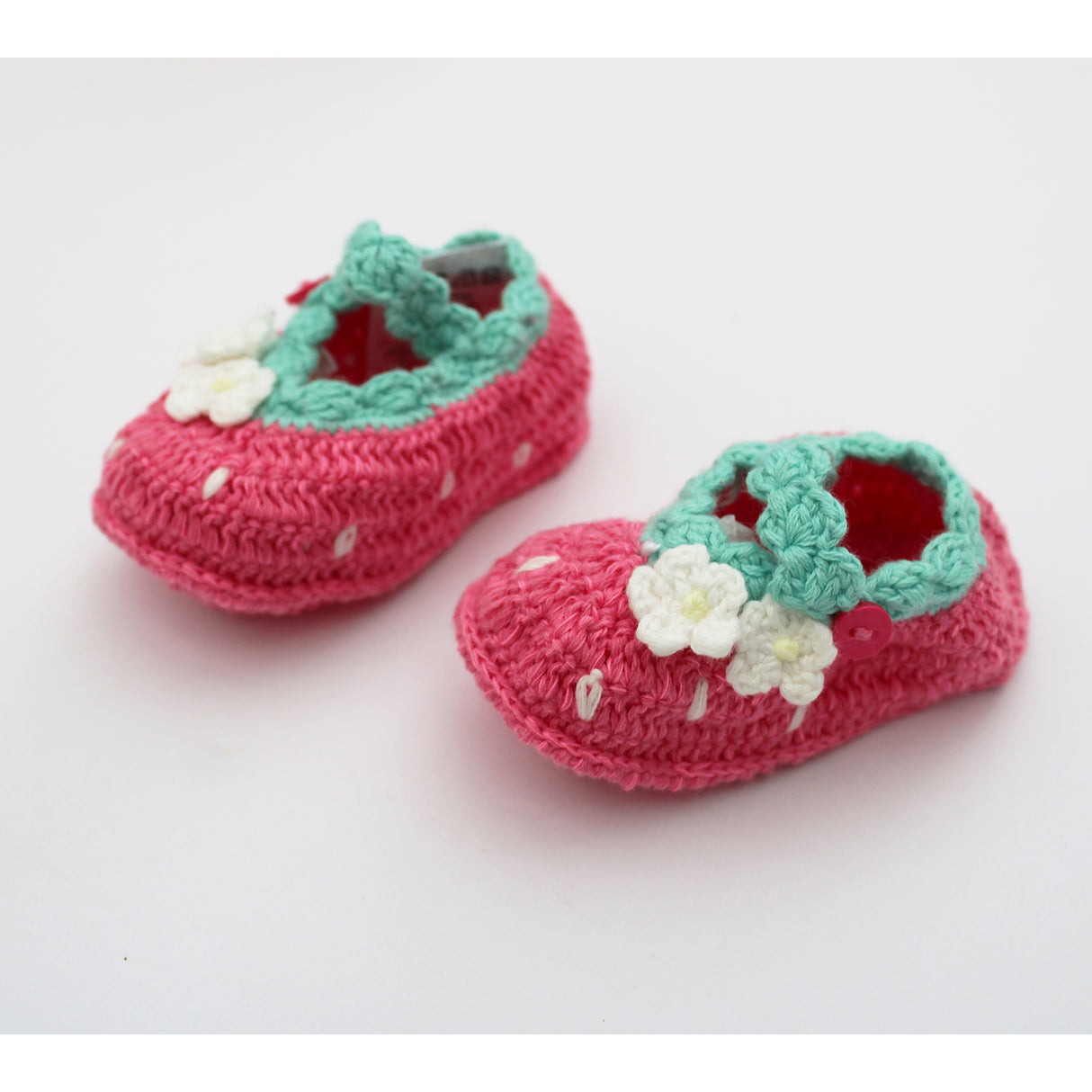 Pair of pink crochet baby shoes with green trim and white flowers on a light gray background