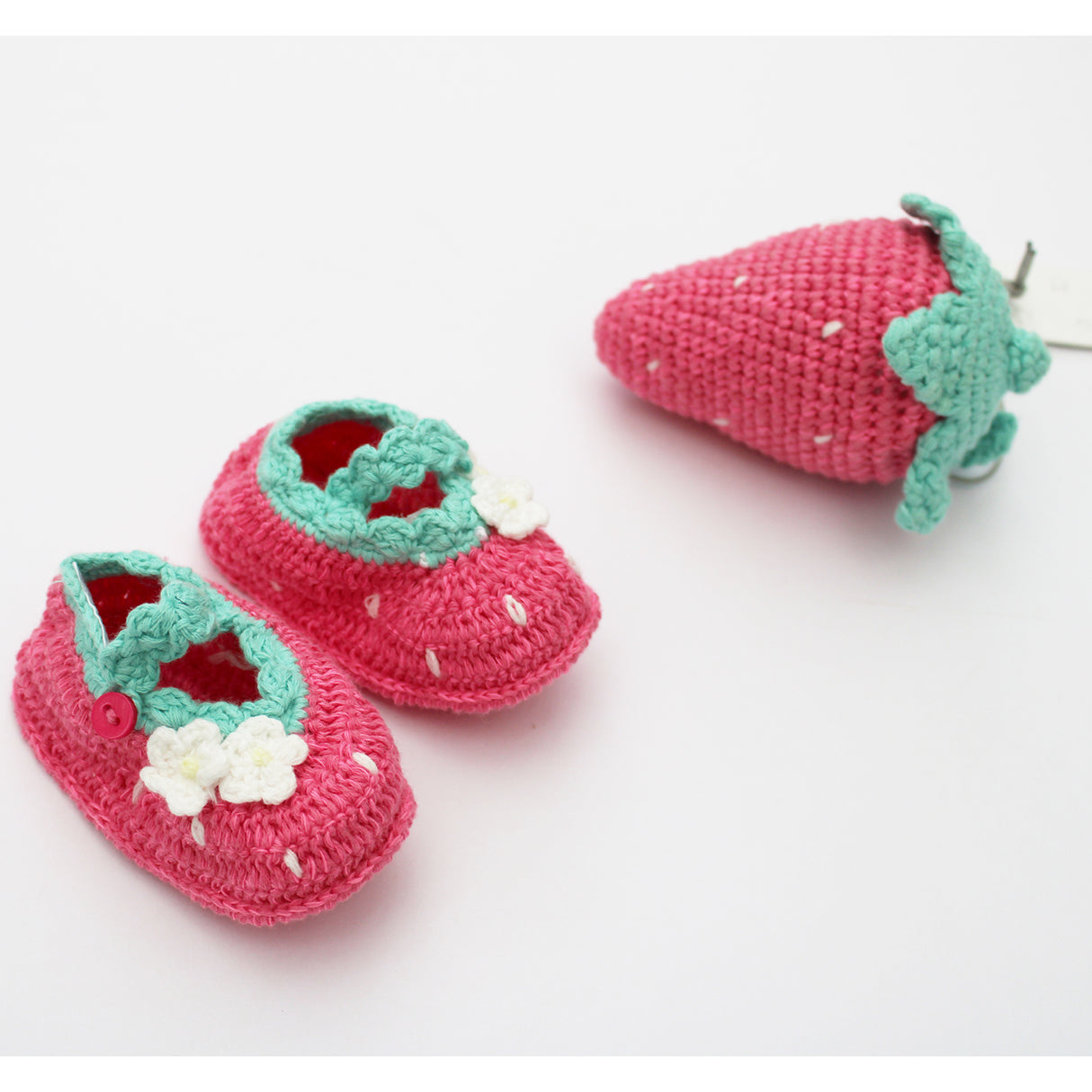 Pink crochet baby shoes with green accents and a matching strawberry on a white background