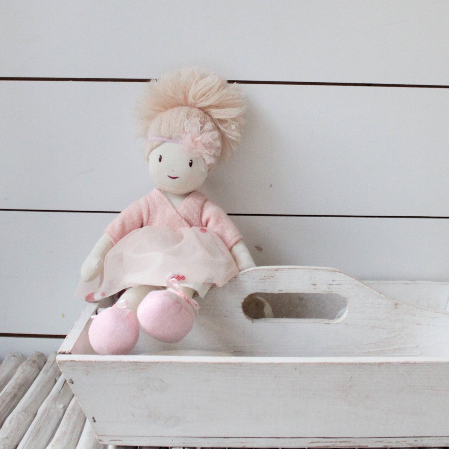 Stuffed rag doll with pink outfit and blonde hair on a white wooden surface