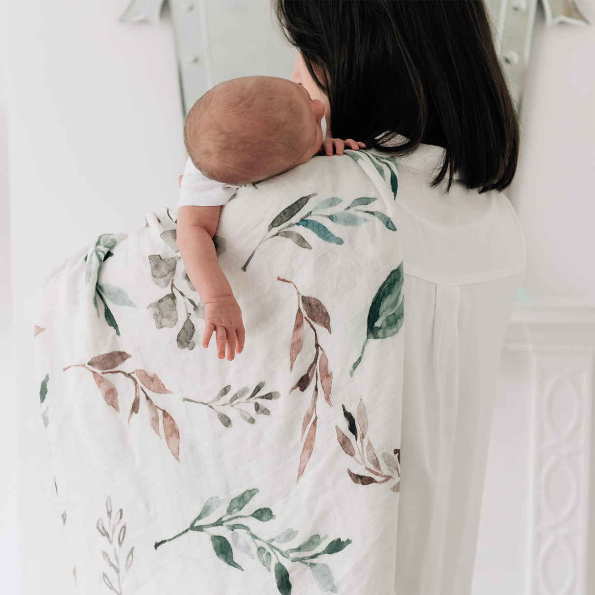 Woman holding a baby wrapped in a botanical blanket against a white background