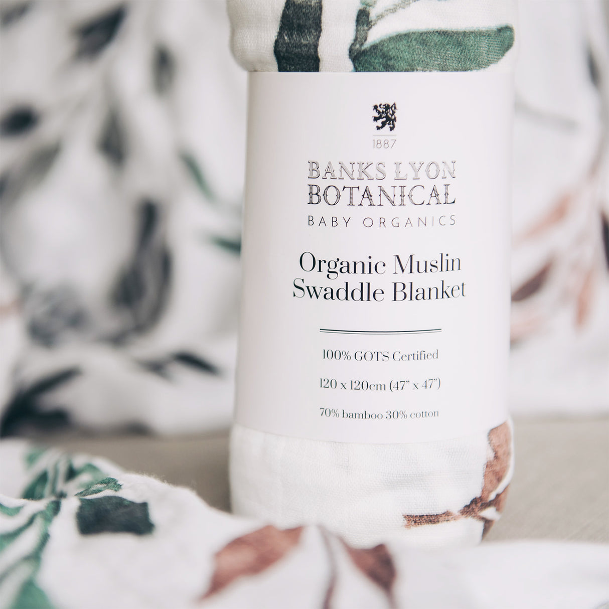 Banks Lyon Botanical Organic Muslin Swaddle Blanket packaging with a blurred background of the product.