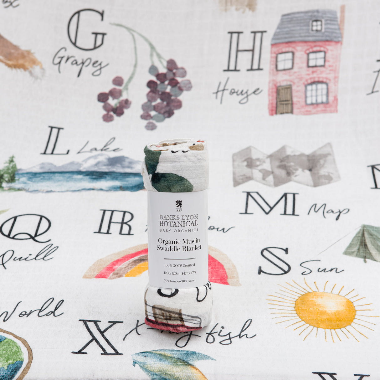 Banks Lyon Botanical Organic Muslin Swaddle Blanket on a decorative fabric background with illustrations and text.