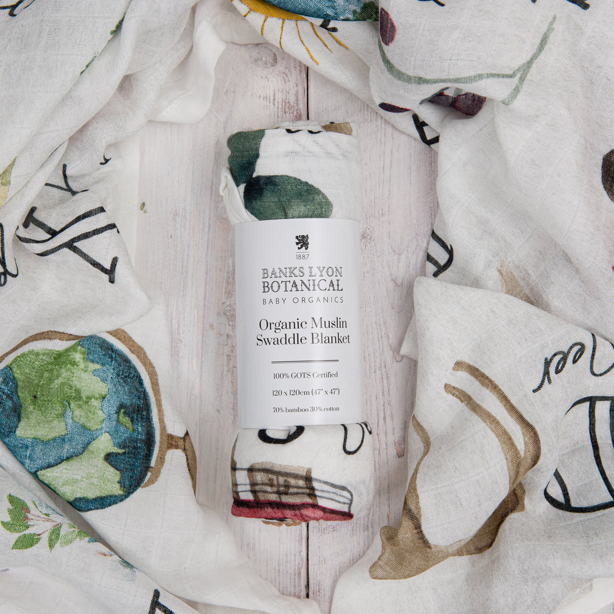 Banks Lyon Botanical Organic Muslin Swaddle Blanket with artistic designs on a wooden surface.
