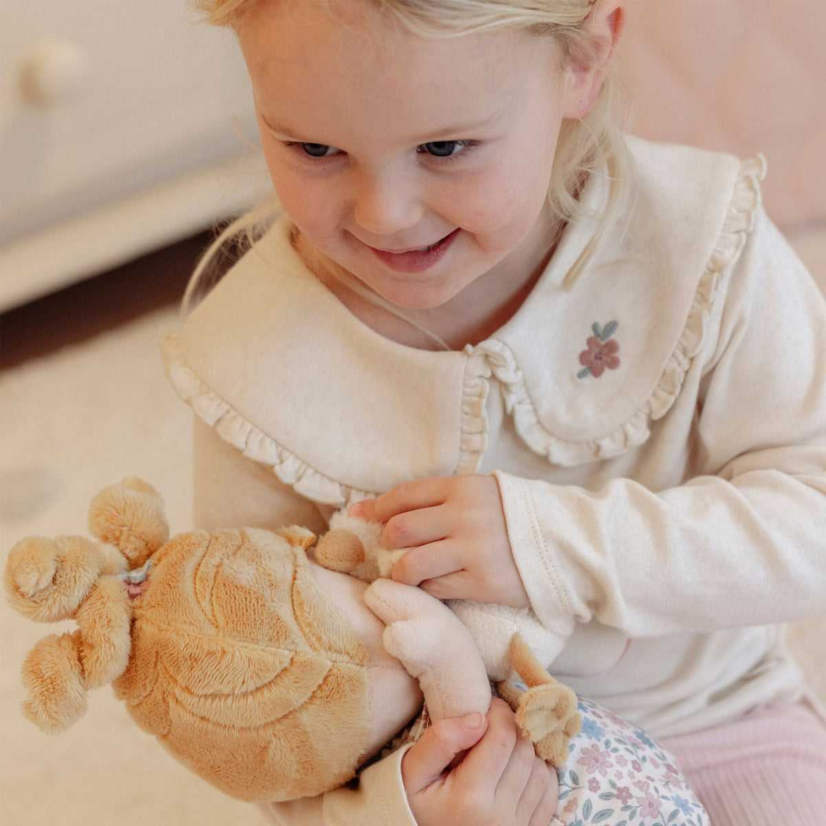 A young blonde girl smiling while holding soft rag doll baby Julia