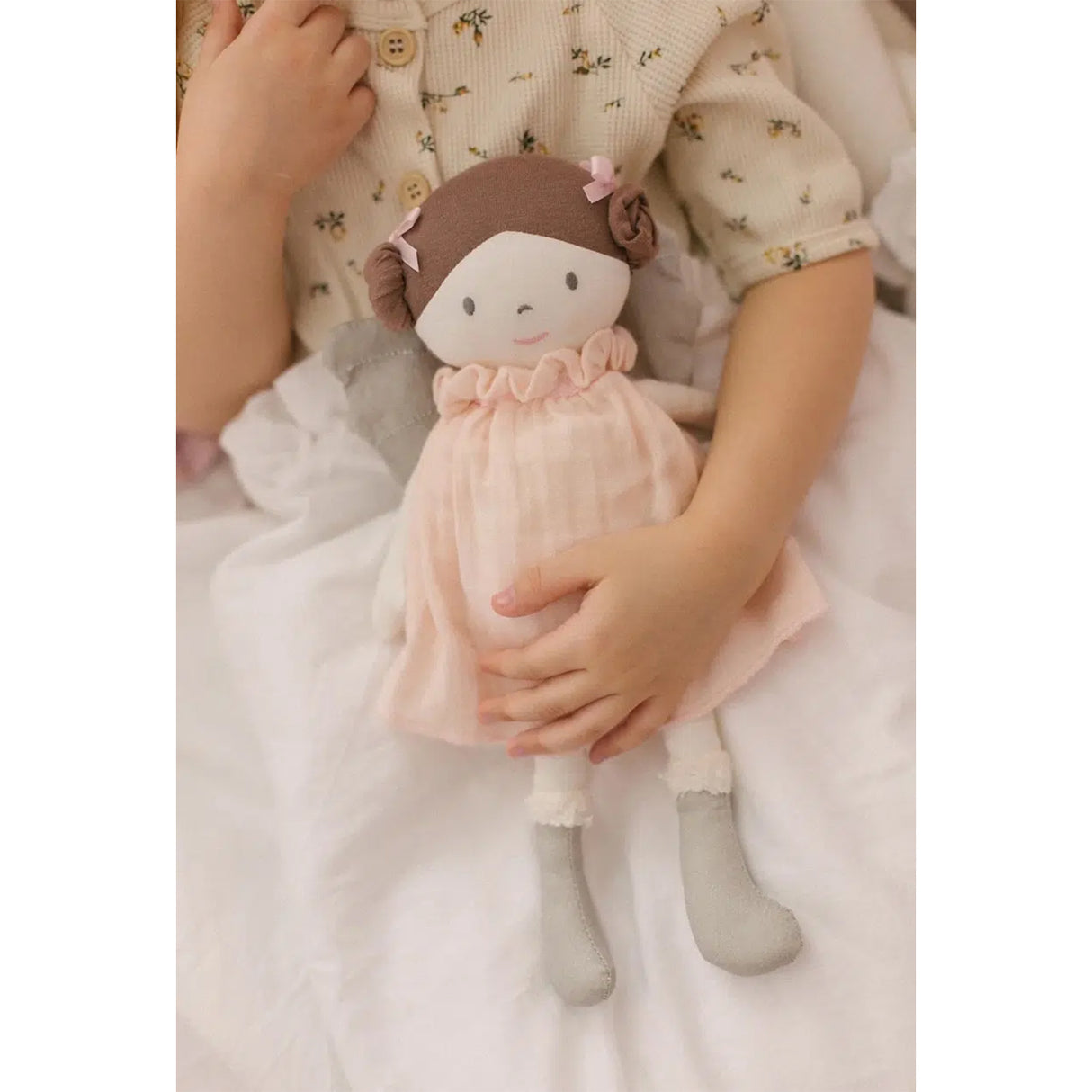 Child holding a soft rag doll fairy toy with a pink dress and brown hair on a white blanket