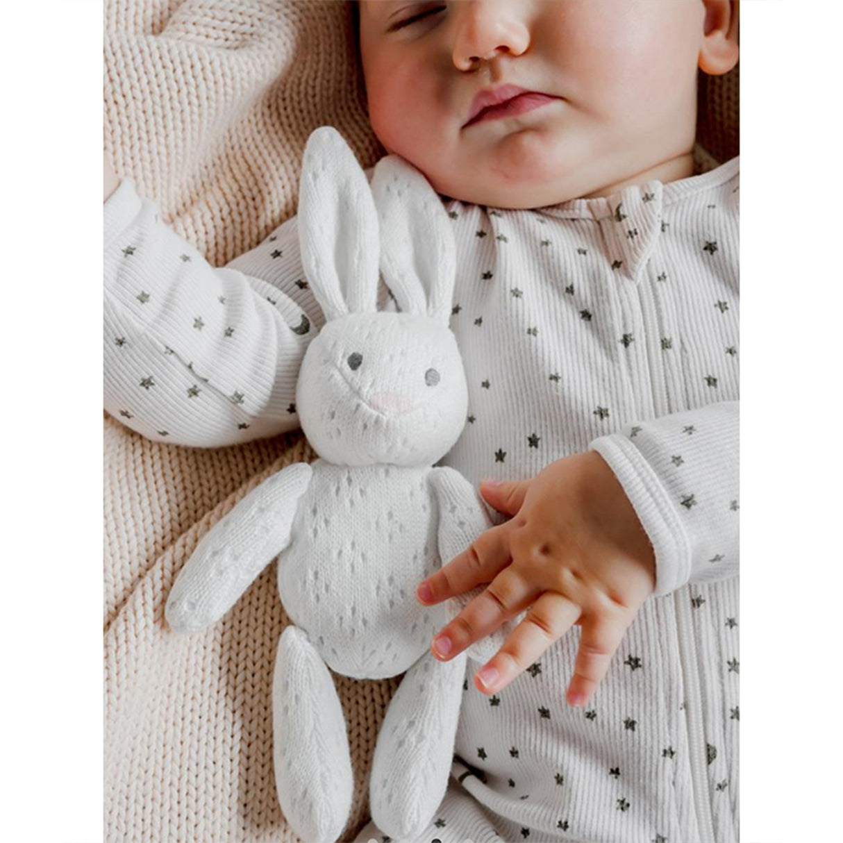 Baby sleeping holding a soft bunny toy with a neutral background