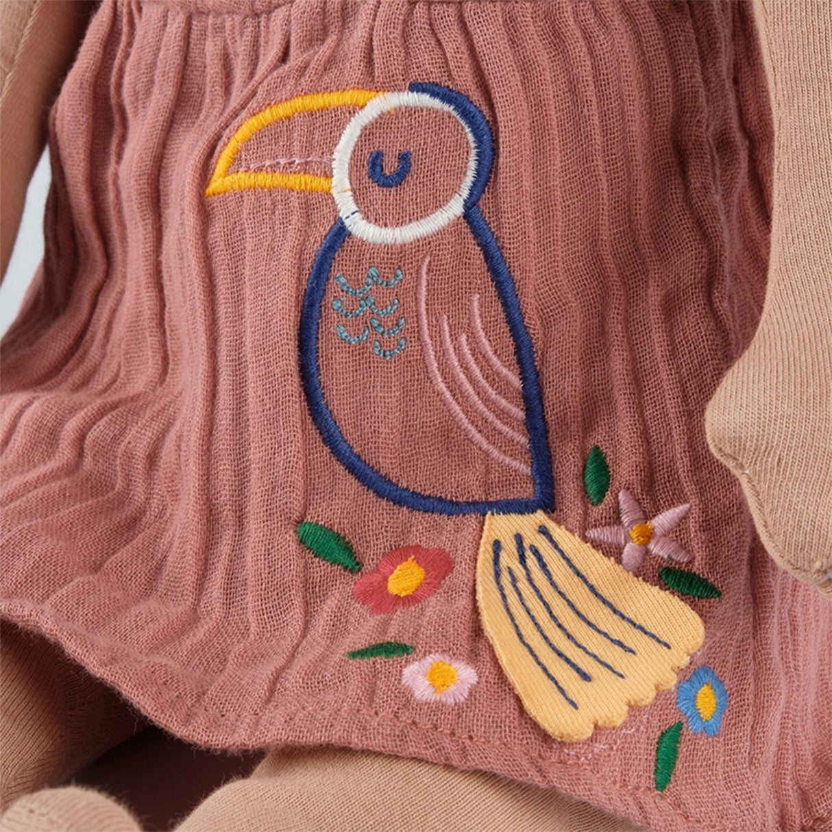 Embroidered toucan design on a pink fabric with flowers.