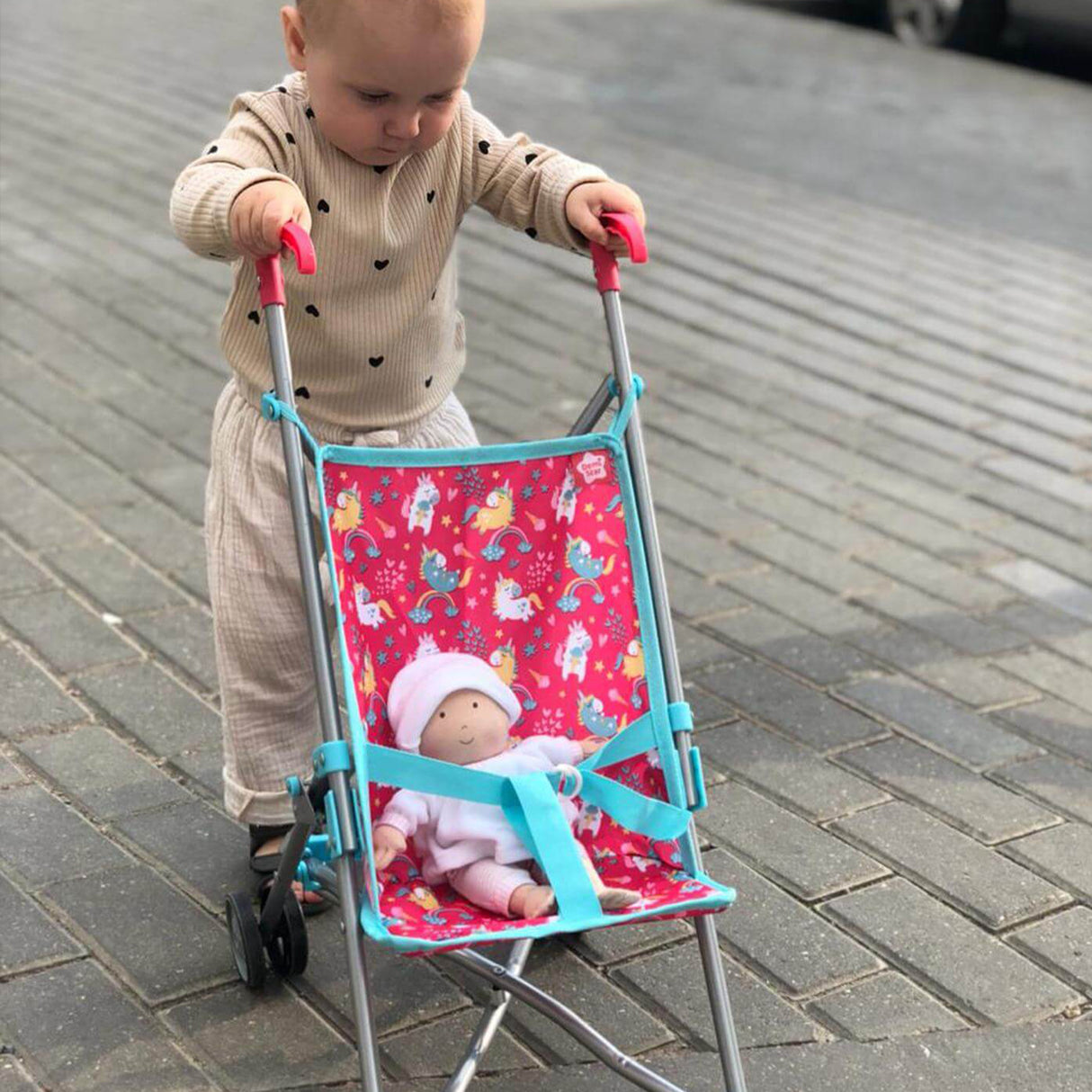 Child pushing a toy stroller with a doll inside on a path.
