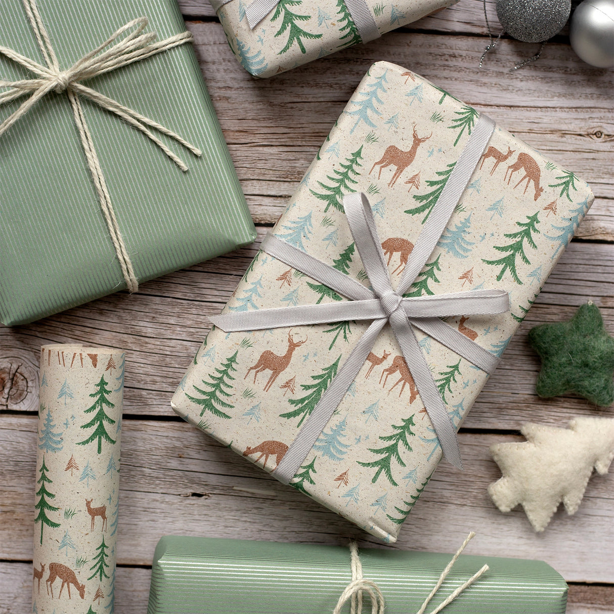 Gifts wrapped in festive paper with deer and tree patterns on a wooden surface.