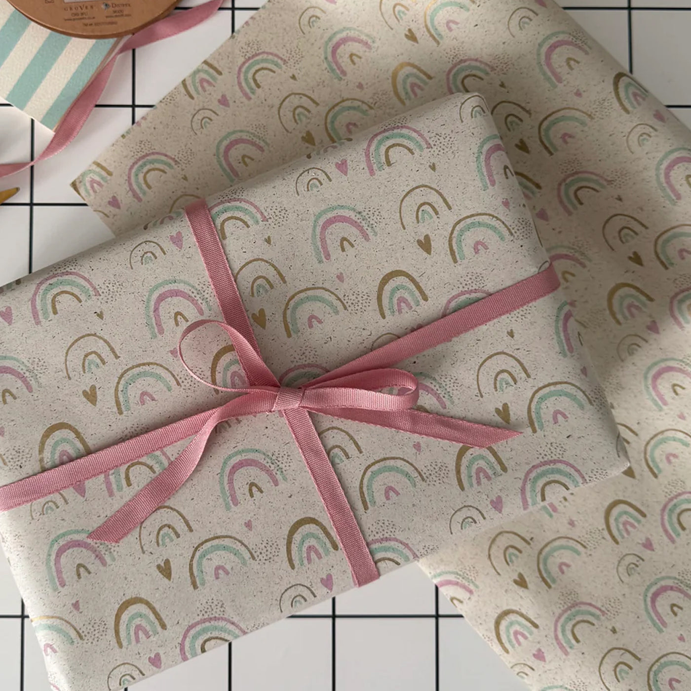 Gift wrapped in rainbow-patterned paper with a pink ribbon on a tiled surface