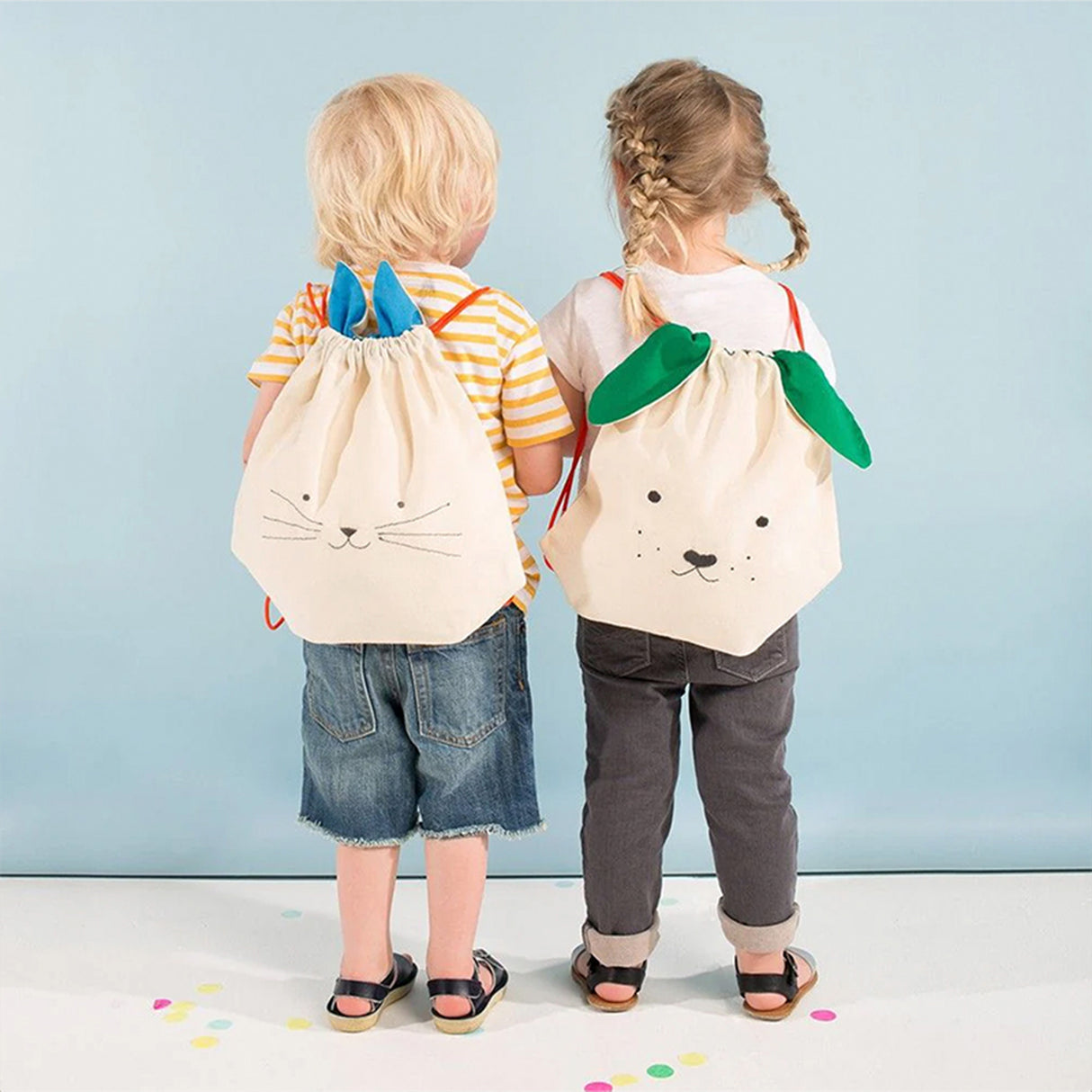 Two children wearing drawstring bags with animal designs against a light blue background