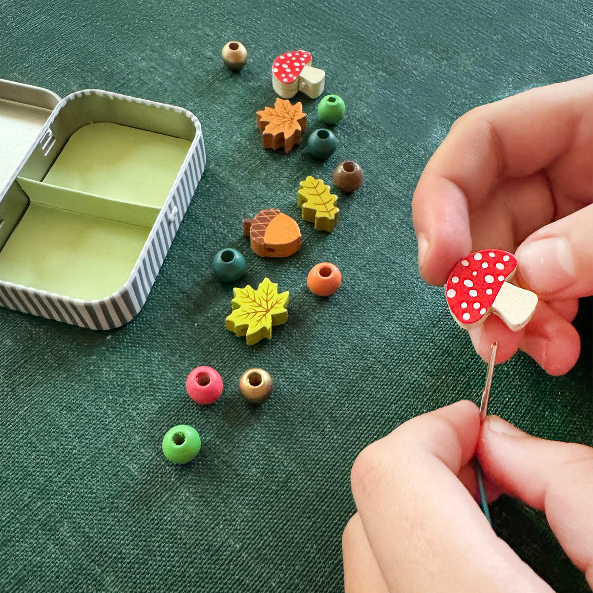 Colorful wooden beads on a green fabric surface with a hand holding a red and white mushroom-shaped bead.