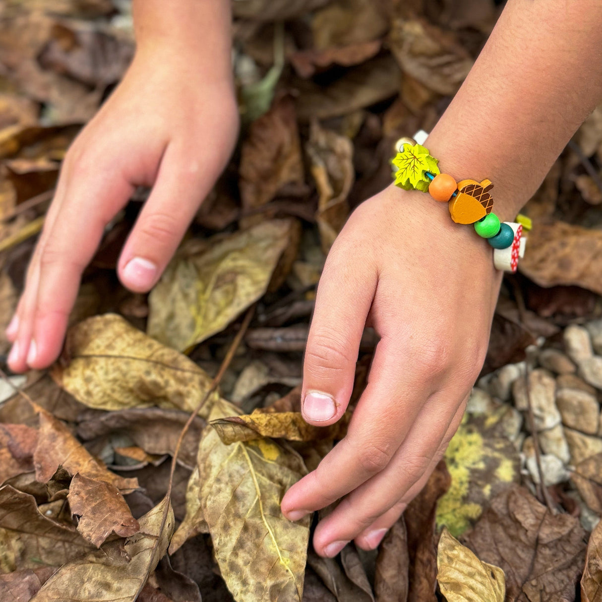 Child's hands on dry leaves with a colorful bracelet