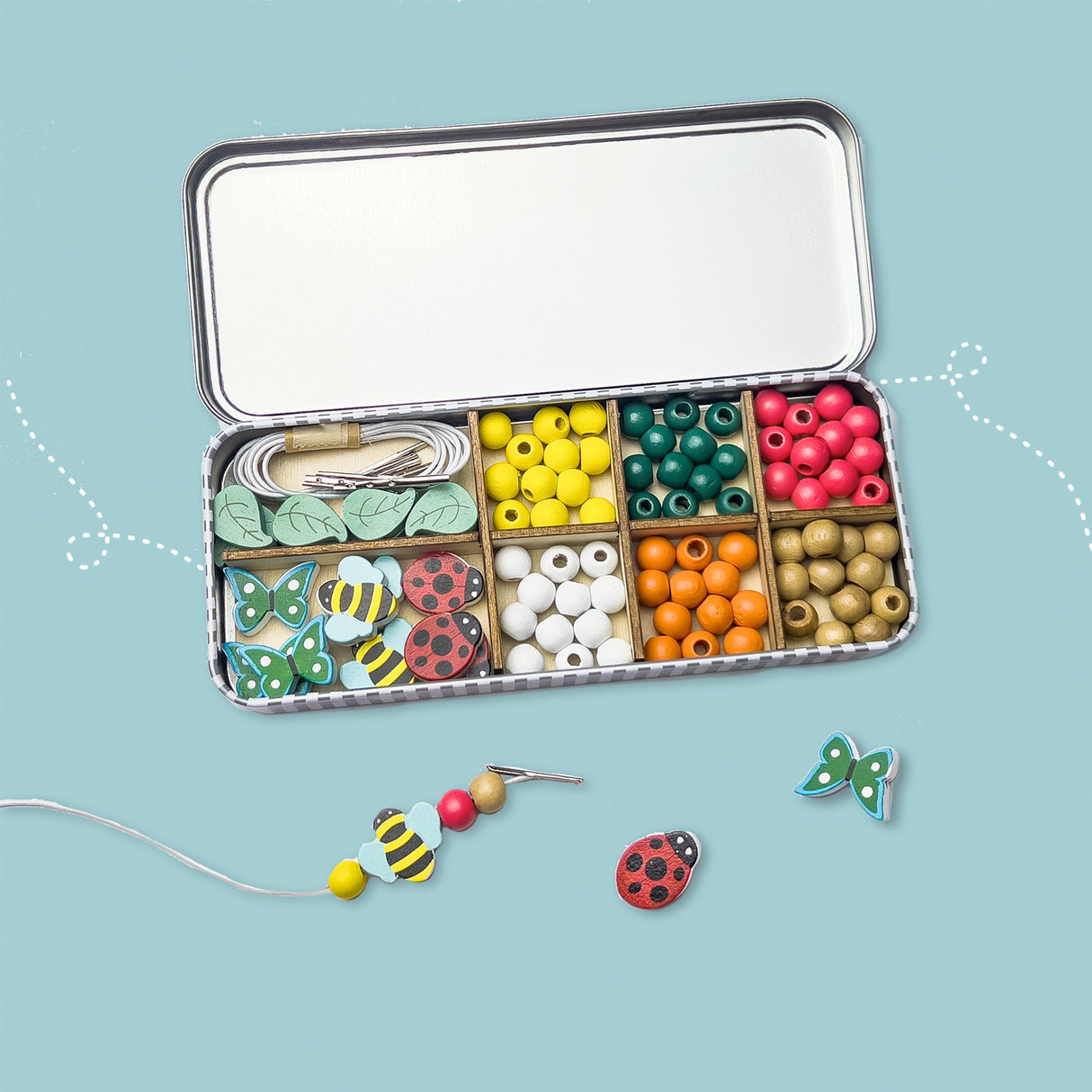 Cotton Twist open tin box with compartments containing colourful beads and decorative items on a blue background