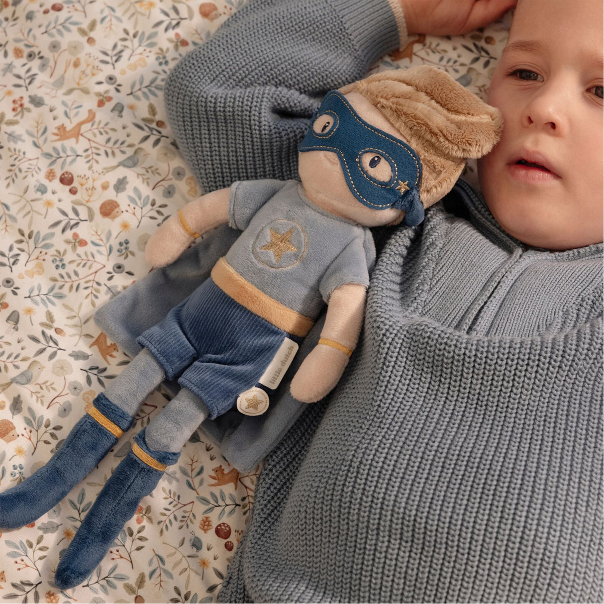 Child holding a plush Jim toy doll with a superhero outfit on a patterned surface