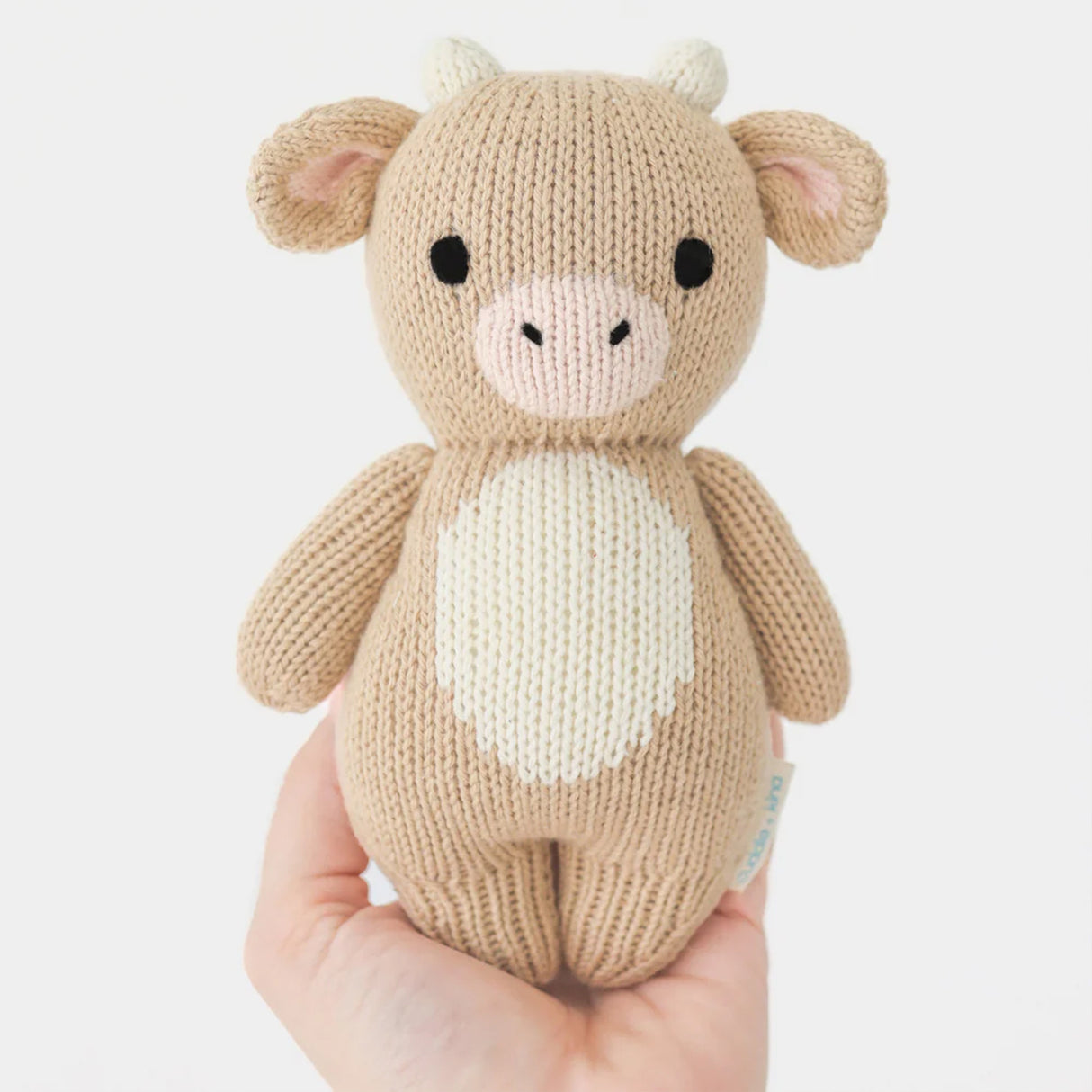 Knitted Baby Jersey cow toy held in a hand against a white background