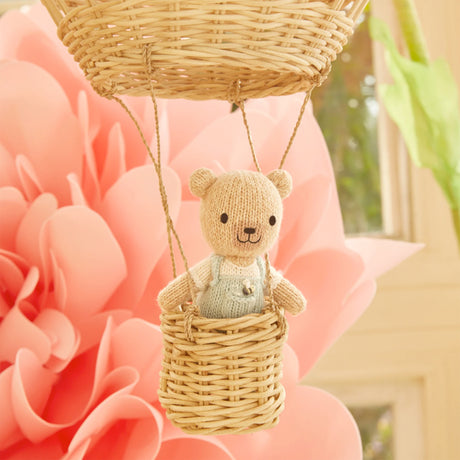 Knitted teddy bear in a wicker basket against a pink floral background