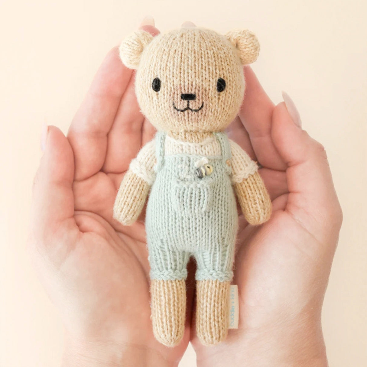 Knitted teddy bear toy held in hands against a beige background