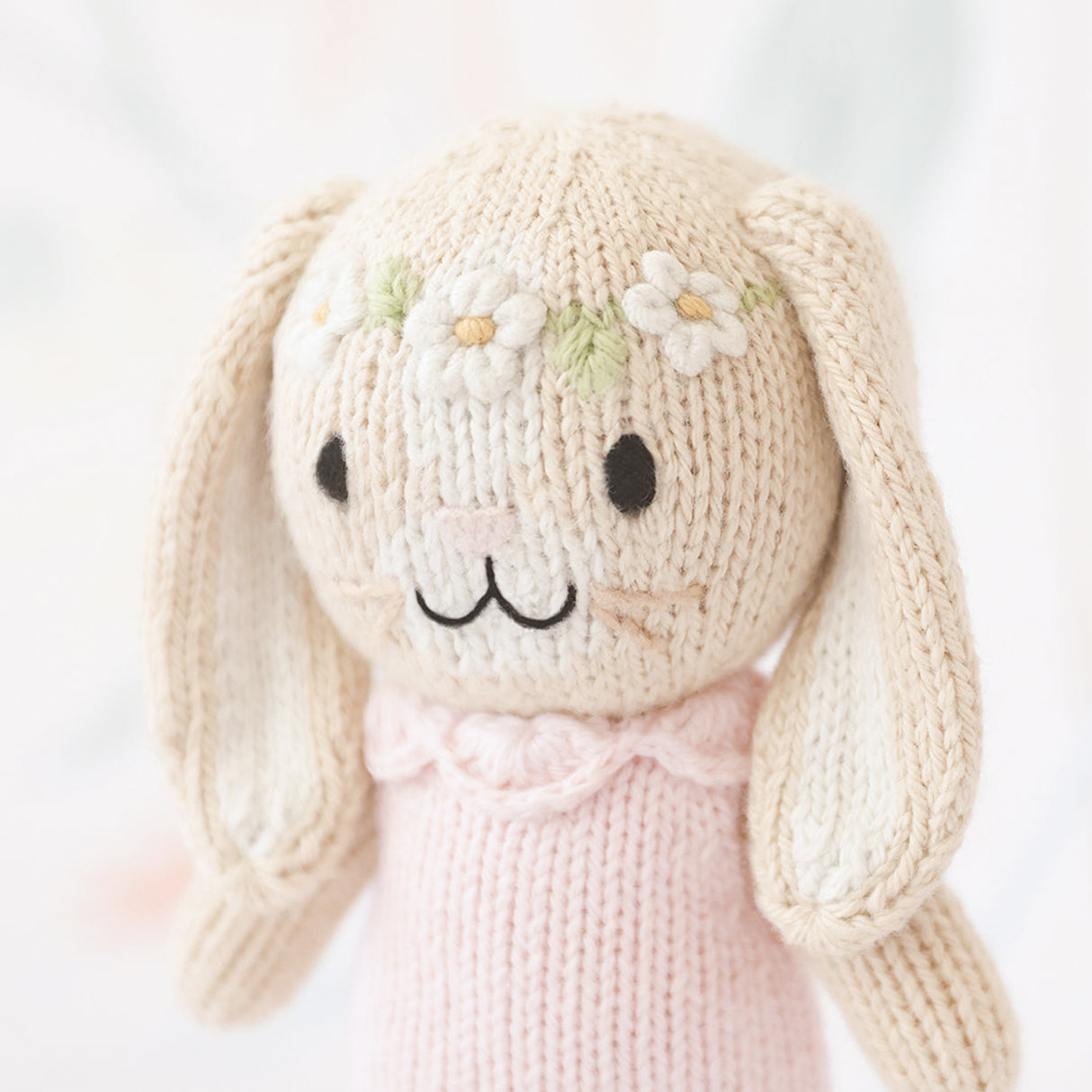 Knitted bunny toy with a pink dress and daisy chain on a white background