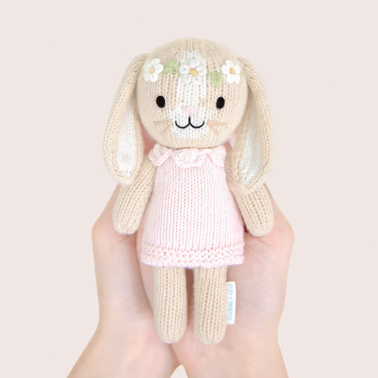 Hand Knitted bunny toy with a pink dress in front of a floral-patterned box on a white background