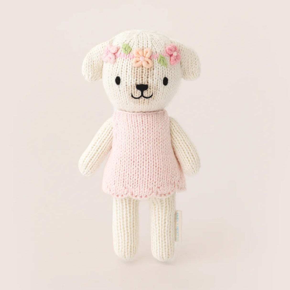 Knitted teddy bear toy with a pink dress and floral decorations on a light background