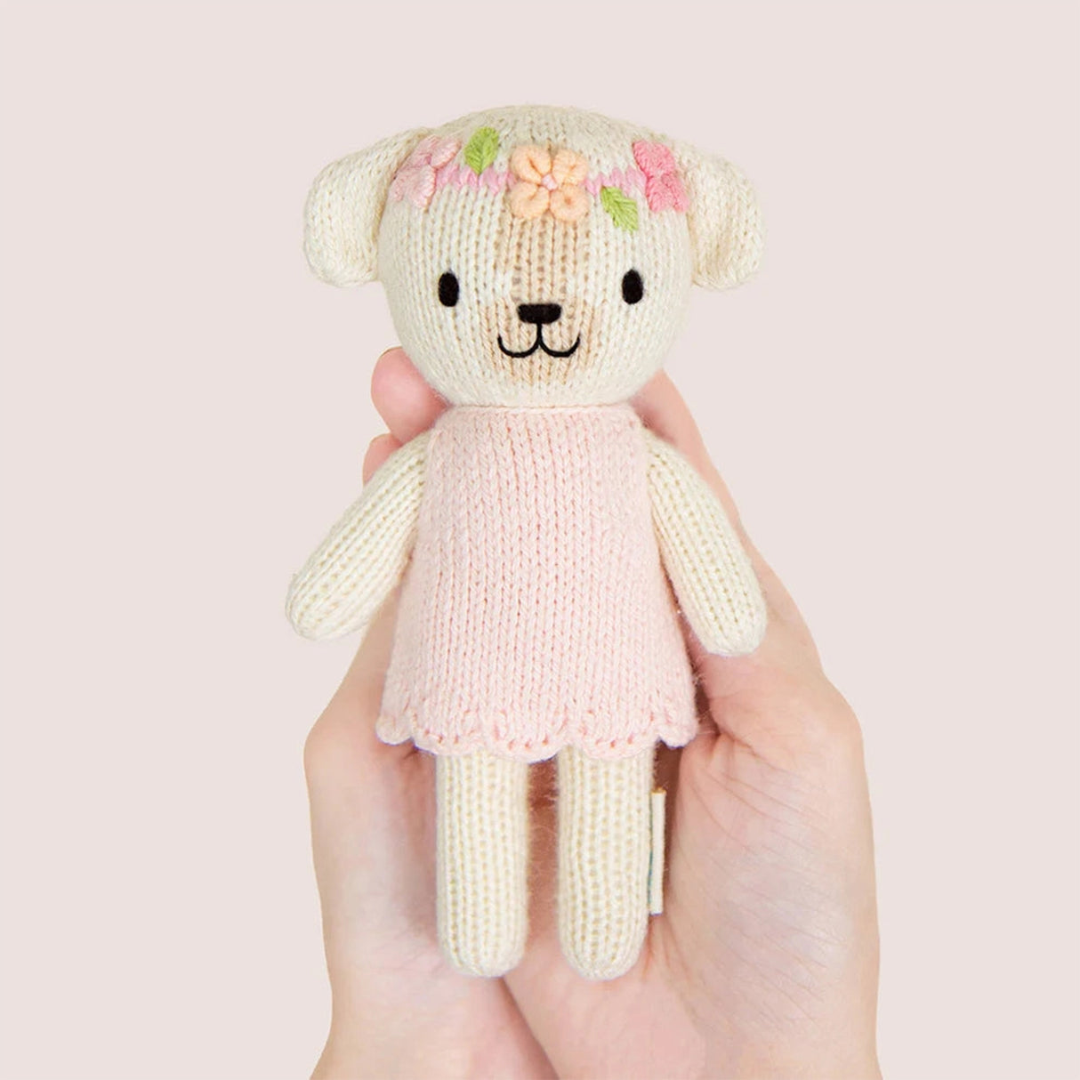 Knitted dog with a pink dress held in a hand against a light pink background