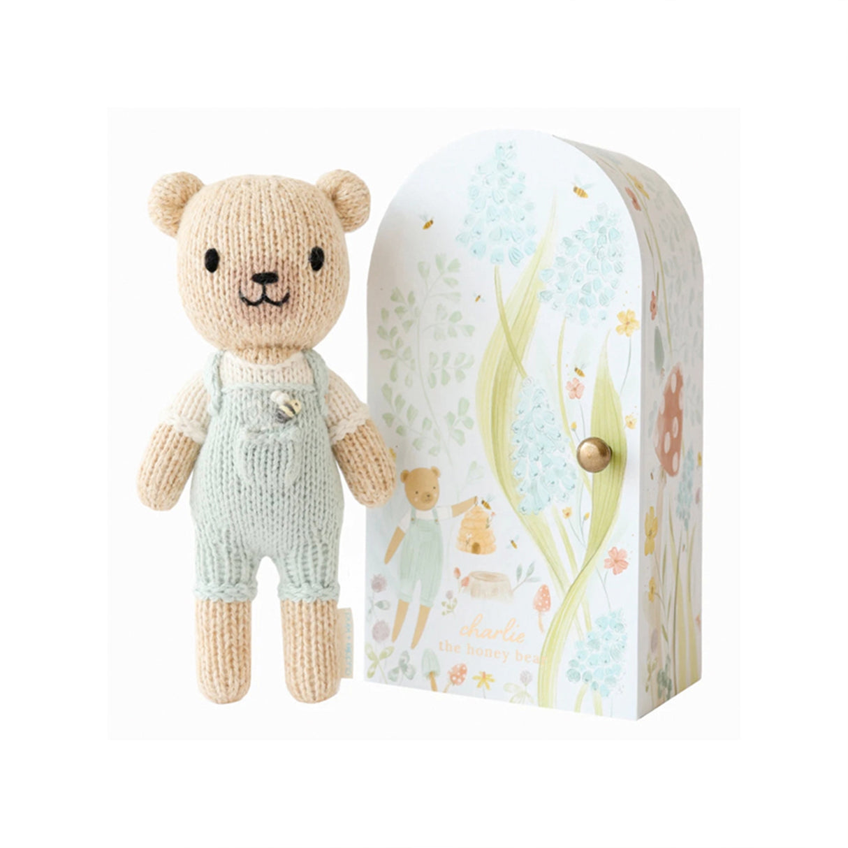 Knitted teddy bear in overalls next to a decorative box with floral patterns