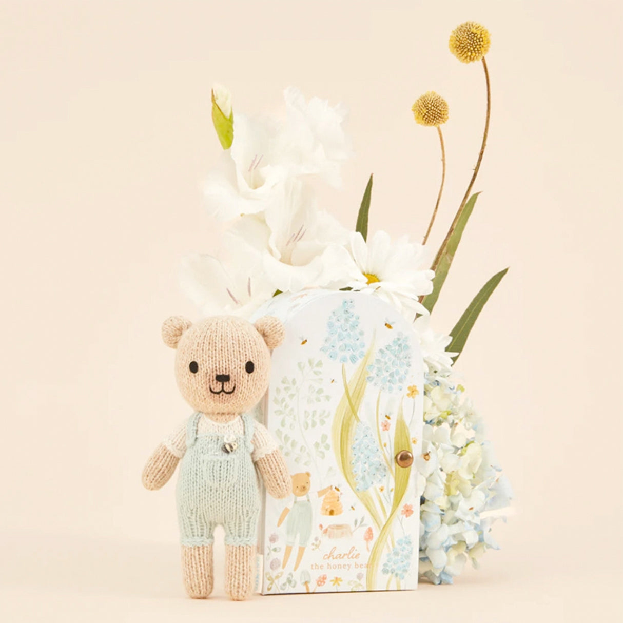 Knitted teddy bear next to a box with a floral design on a light beige background