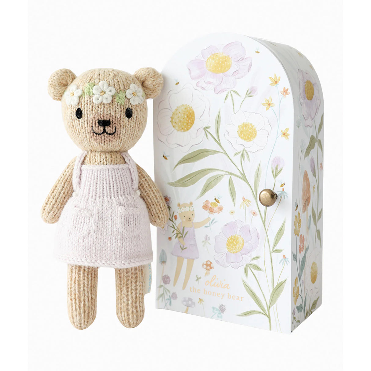 Knitted teddy bear in a dress with a floral headband next to a decorative box with floral design.