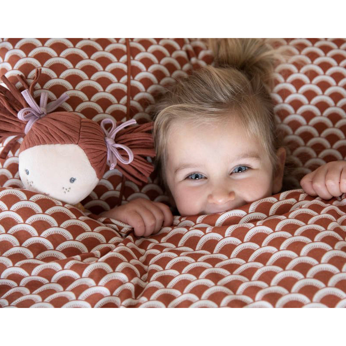 Child lying on a patterned blanket with a soft doll next to them