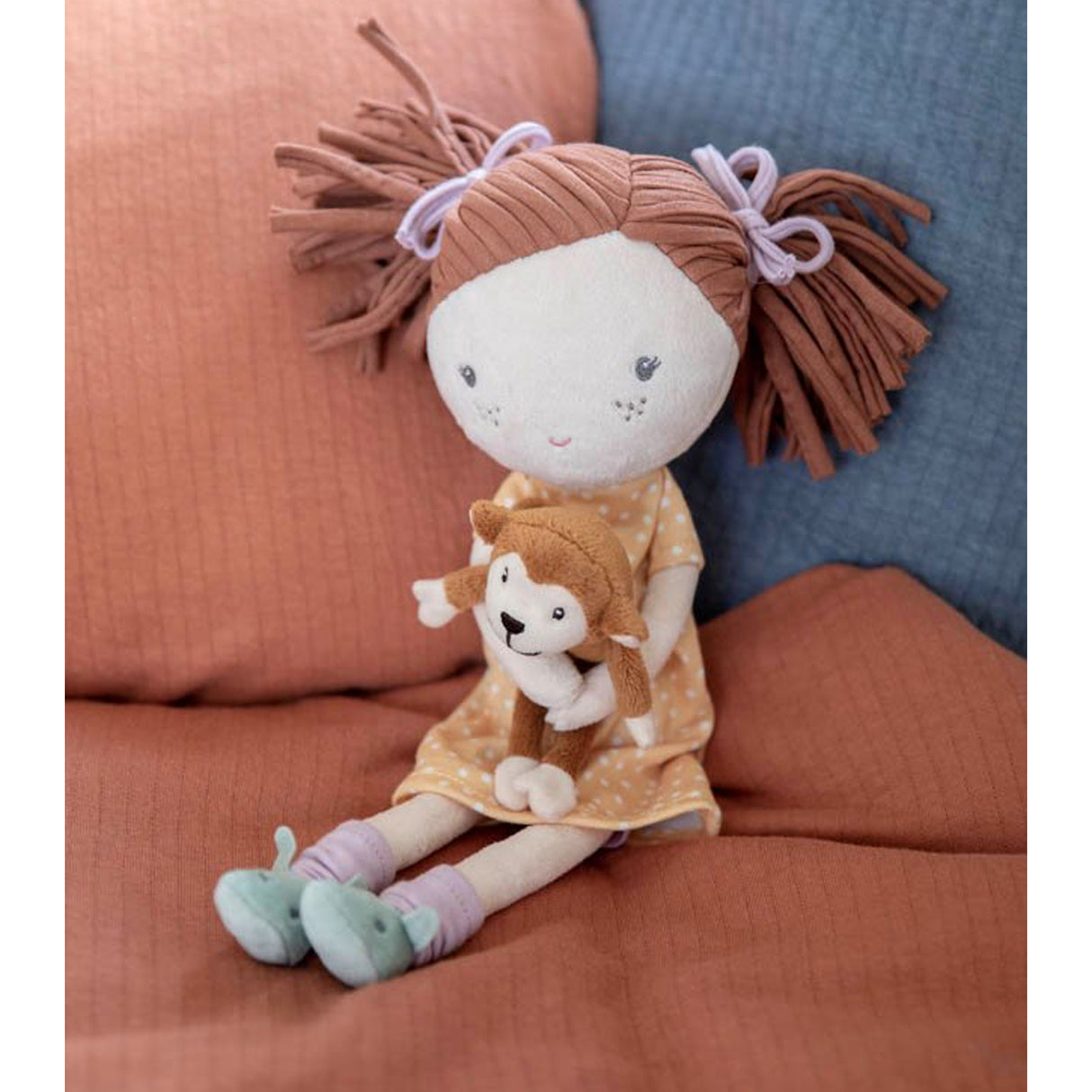 Rag doll with brown hair and a monkey plushie on a soft surface
