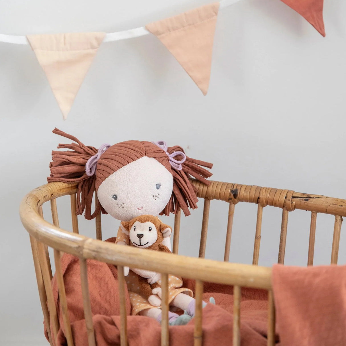 Stuffed soft doll with brown hair and a lmonkey plush in a crib with brown bedding.