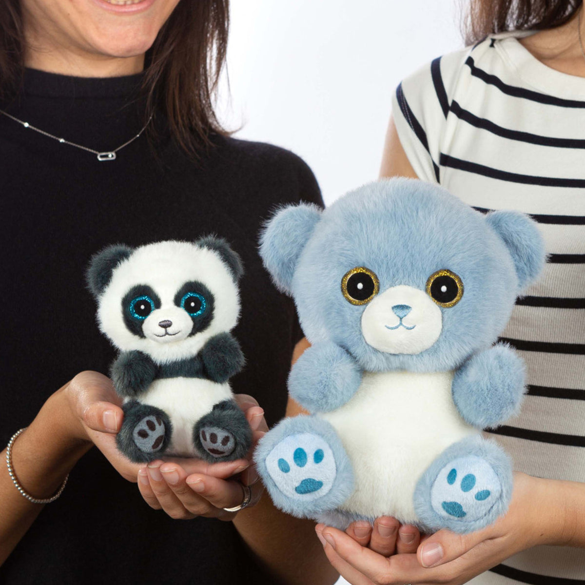 Two plush stuffed animals being held in hands: a small black-and-white panda with blue eyes on the left, and a larger light blue bear with a white belly on the right.
