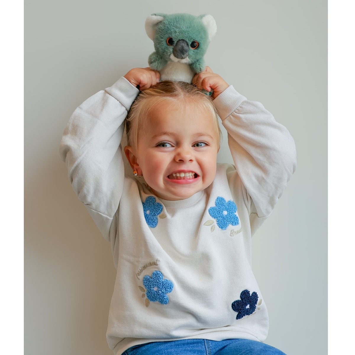 Young girl balancing Gipsy Toys Cutydoos Koala plush toy on her head and laughing