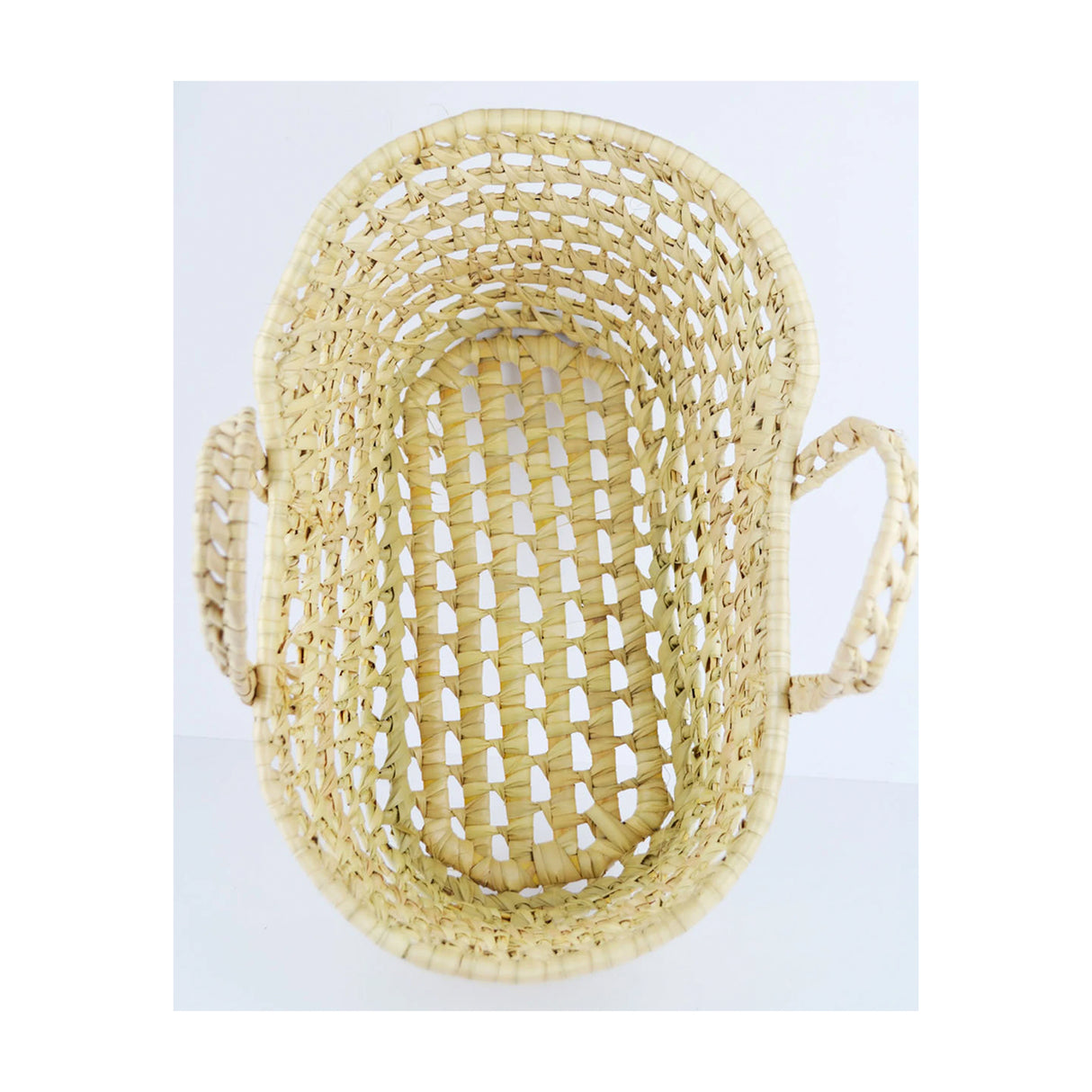 A beige wicker bassinet or moses basket with two side handles, suitable for carrying dolls or soft toys.