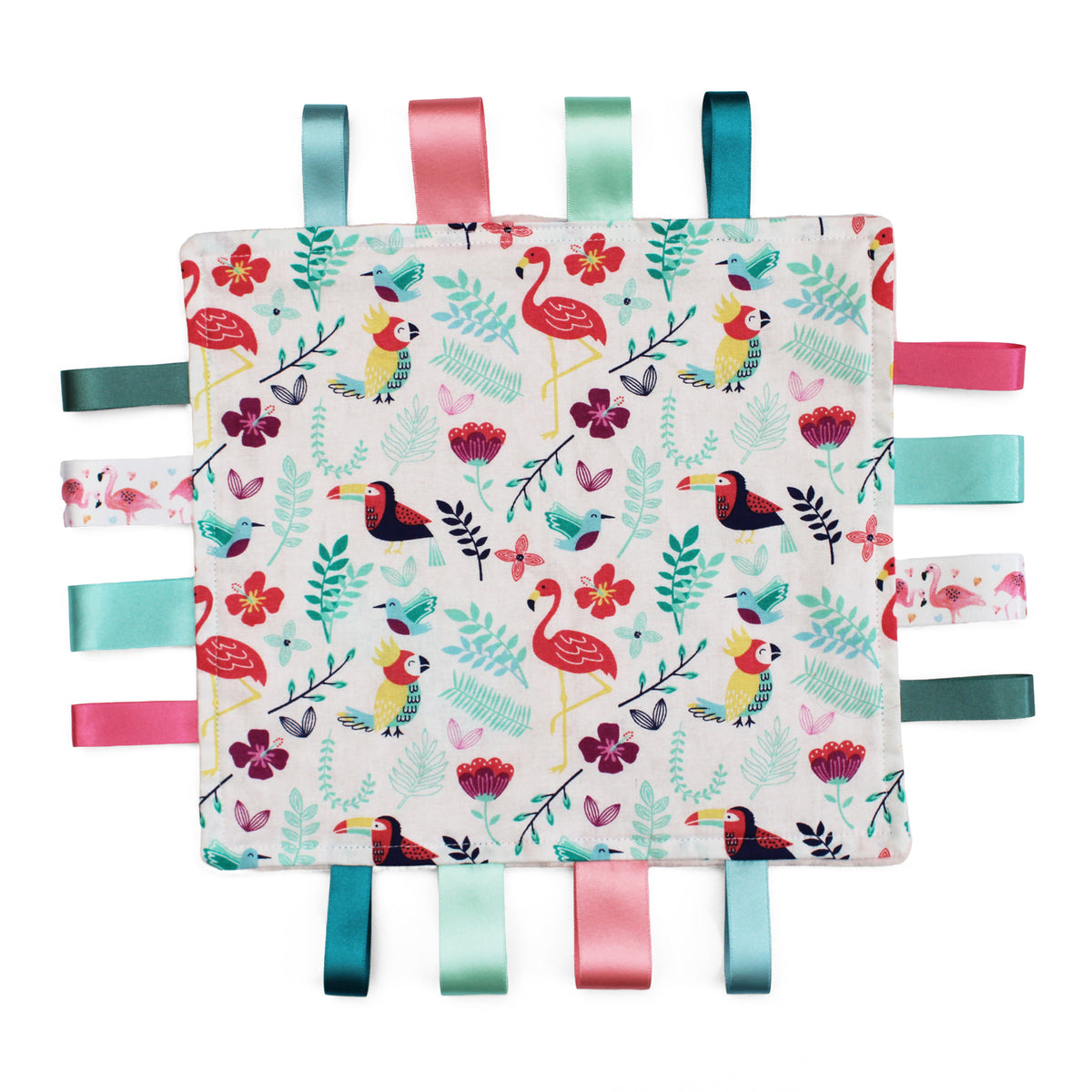 A square fabric sensory baby soother with a colourful tropical pattern featuring flamingos, toucans and leaves on a white background, finished with eight hanging ribbon tabs in teal, pink, mint, and dark green.