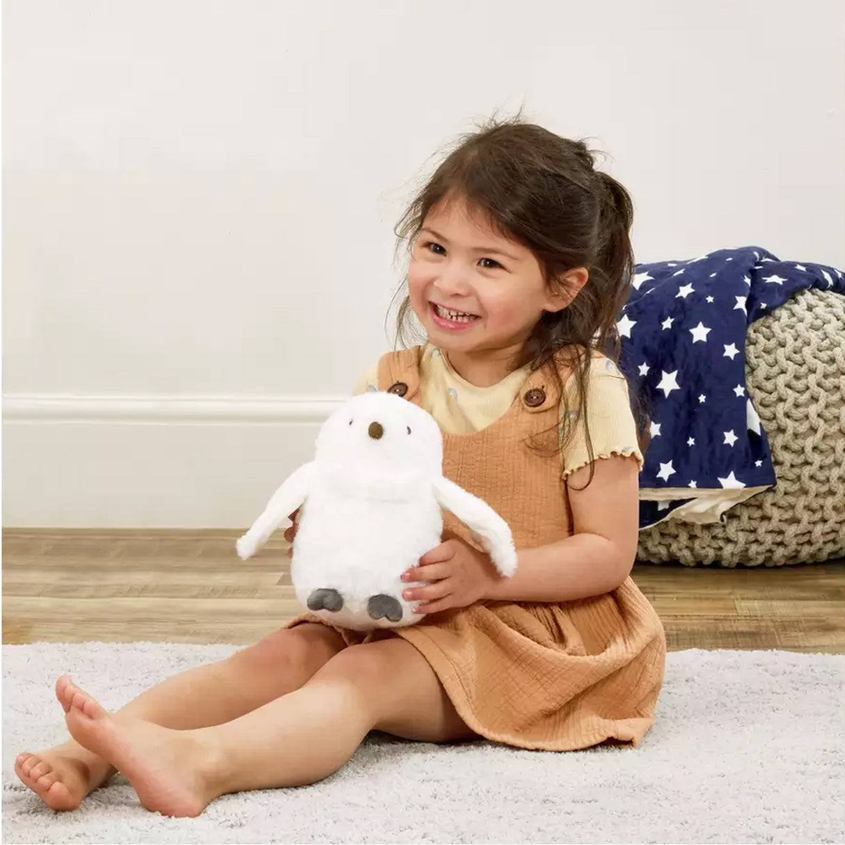 Child holding a plush Harry Potter Hedwig toy on a carpeted floor with a star-patterned blanket in the background