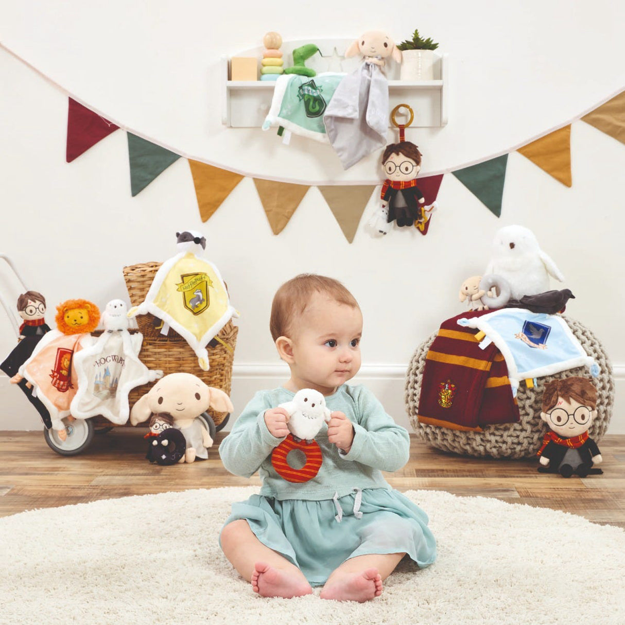 Baby sitting on a rug holding a toy, surrounded by Harry Potter-themed plush toys and decorations.