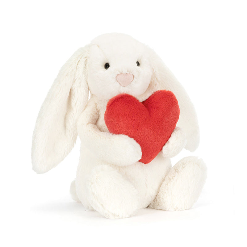 A soft plush toy resembling a white bunny holding a red love heart.
