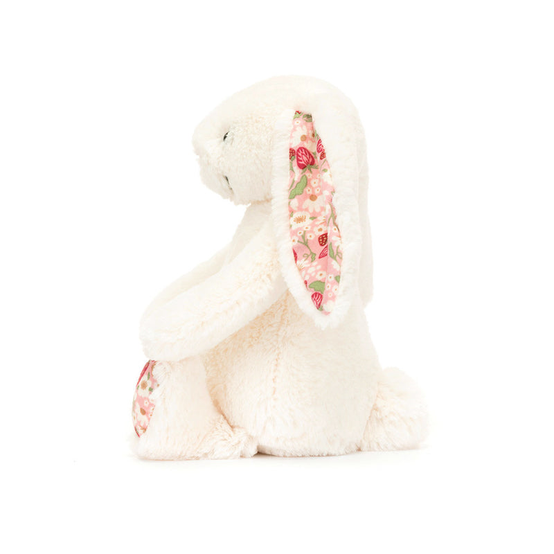 A small plush toy resembling a cream-colored bunny with soft cotton ears and feet, featuring a strawberry and cream flower pattern on a pink backdrop.