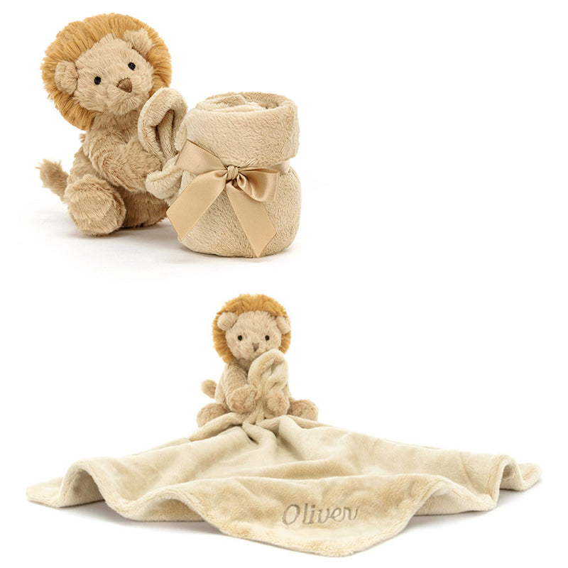 A plush toy depicting a lion with a beige mane and cream-brûlé fur, holding and cuddling a beige soother blanket with the name 'Oliver' printed on it.