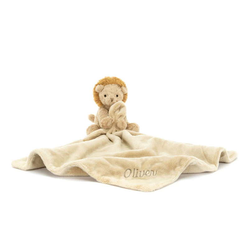 A plush toy depicting a lion with a beige mane and cream-brûlé fur, holding and cuddling a beige soother blanket with the name 'Oliver' printed on it.