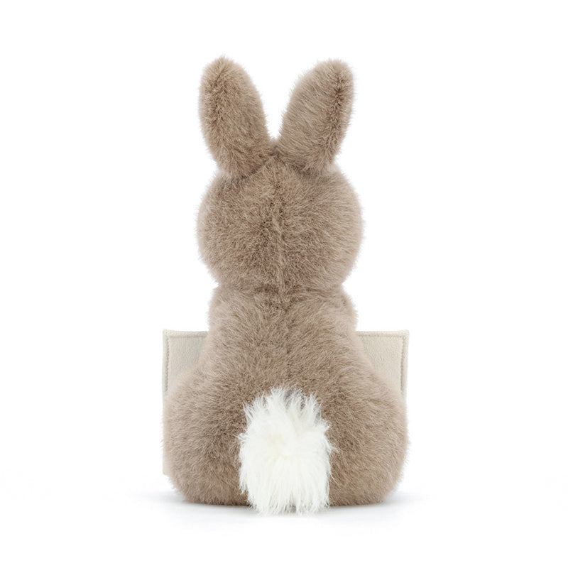 A plush toy resembling a bunny holding a beige envelope with a card.