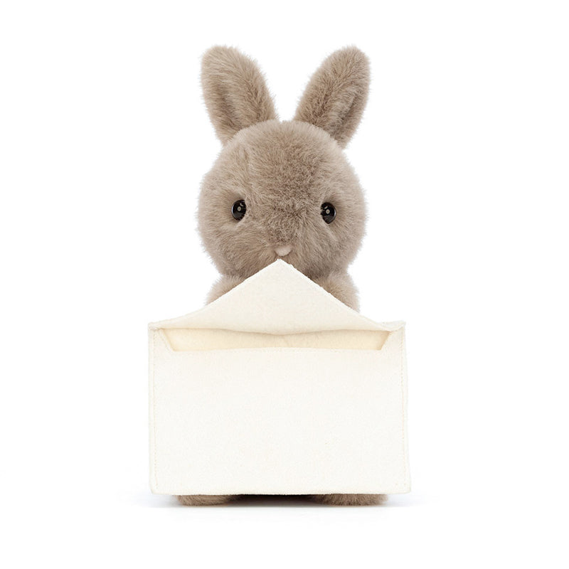 A plush toy resembling a gray bunny holding a beige envelope with a card.