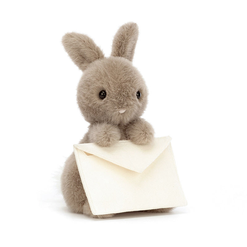 A plush toy resembling a gray bunny holding a beige envelope with a card.