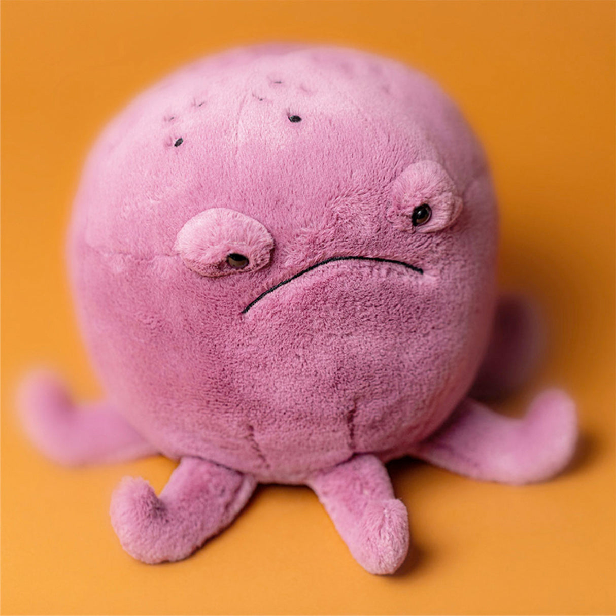 Pink octopus plush toy with a down-turned mouth expression on an orange background