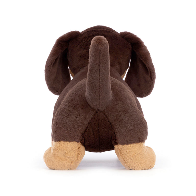 A plush toy resembling a small sausage dog with dark brown fur and light brown patches, featuring waggly ears and a perky tail.