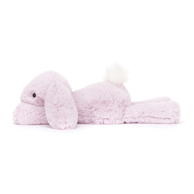 A plush lavender-colored Jellycat Bashful Beige Bunny with a fluffy cream bobtail, lying down.