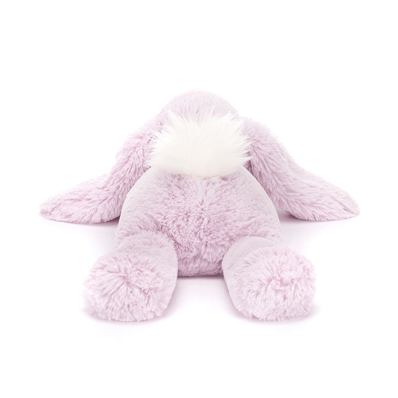A plush lavender-colored Jellycat Bashful Beige Bunny with a fluffy cream bobtail, lying down.